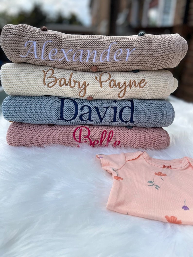 Stack of personalised embroidered baby blankets with custom names in various colours