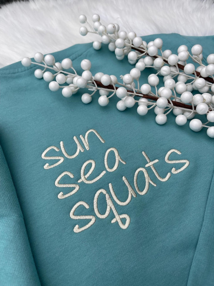 Blue sweatshirt with "sun sea squats" embroidered text