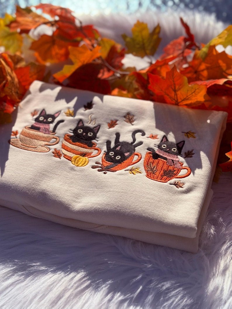 Close-up of milkshake sweatshirt with embroidered black cats sitting in mugs and pumpkins