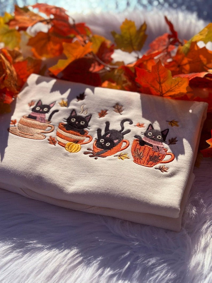Close-up of milkshake sweatshirt with embroidered black cats sitting in mugs and pumpkins