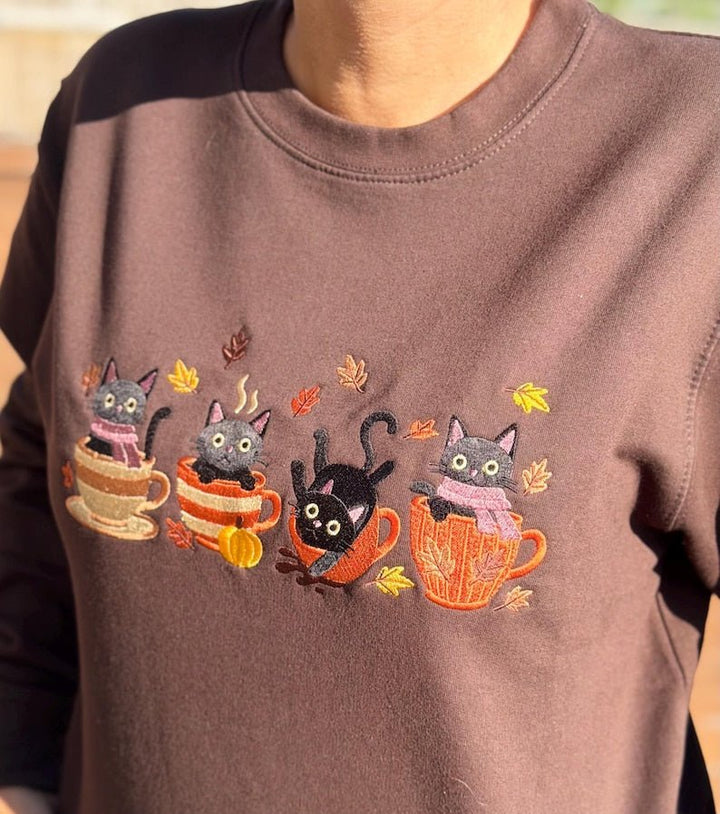 Model wearing brown sweatshirt with embroidered black cats in autumn mugs