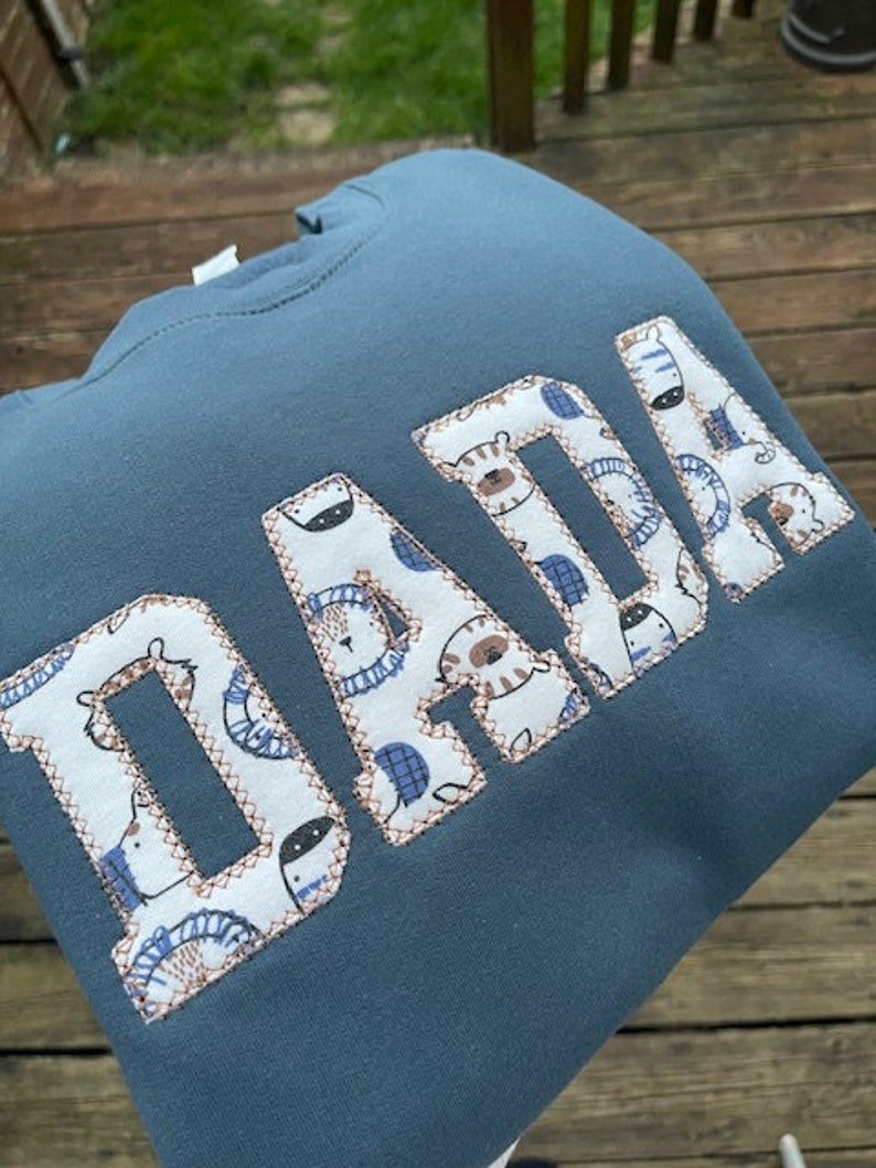 Blue sweatshirt with applique “Dada” in white patterned fabric letters