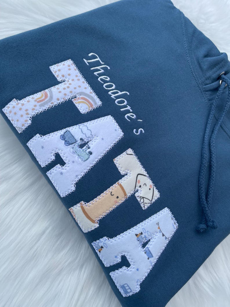 Blue sweatshirt with appliqué “Tata” in white patterned fabric letters