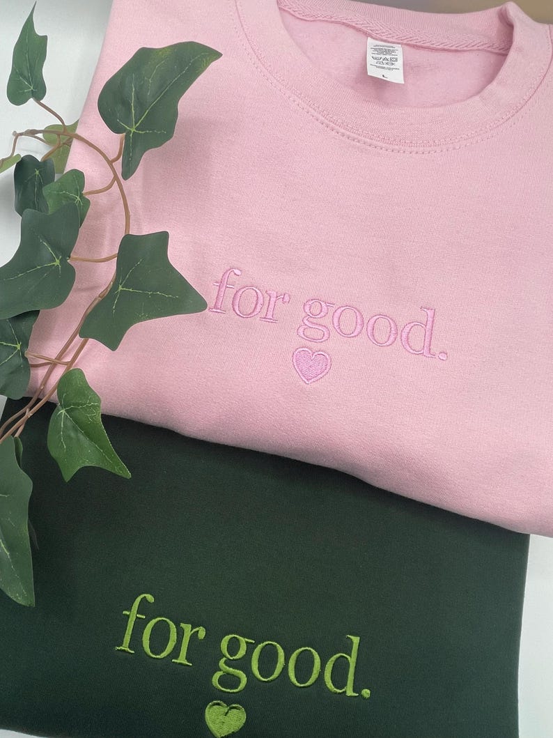 Pink and green embroidered sweatshirts with Wicked “For Good.” text