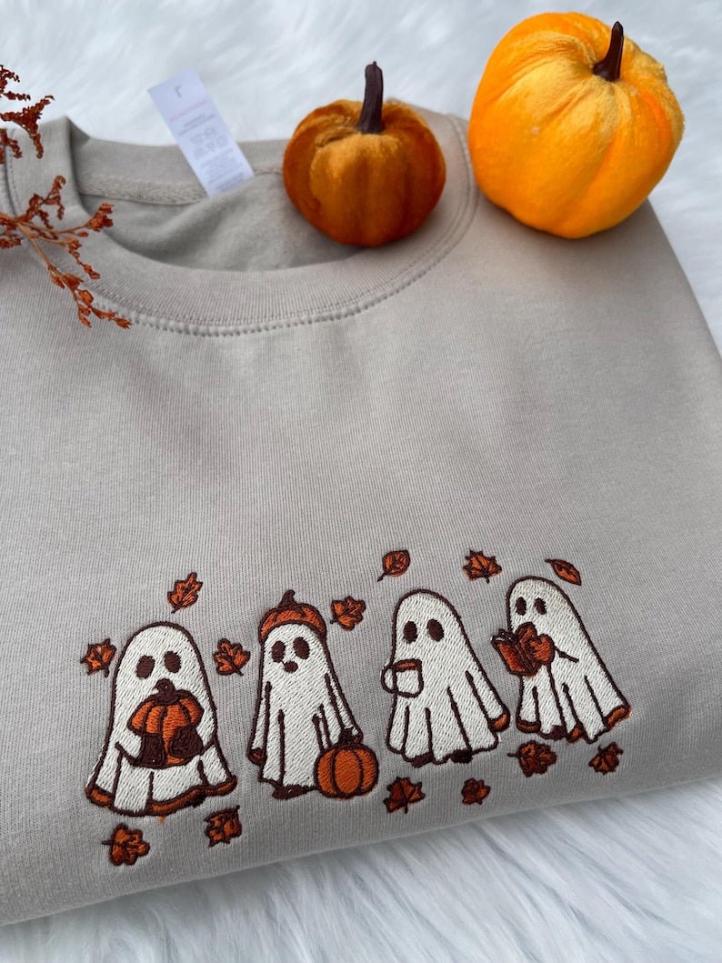 Beige sweatshirt with embroidered Halloween ghost design, styled with pumpkins
