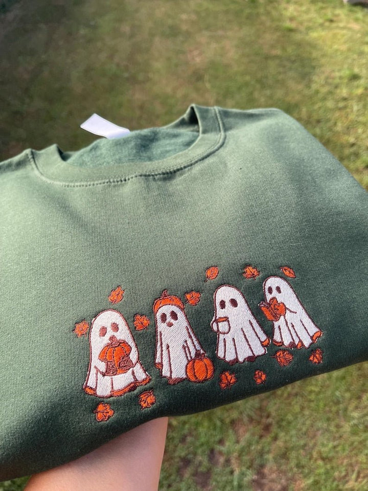 Outdoor shot of green sweatshirt with embroidered line of Halloween ghosts holding pumpkins
