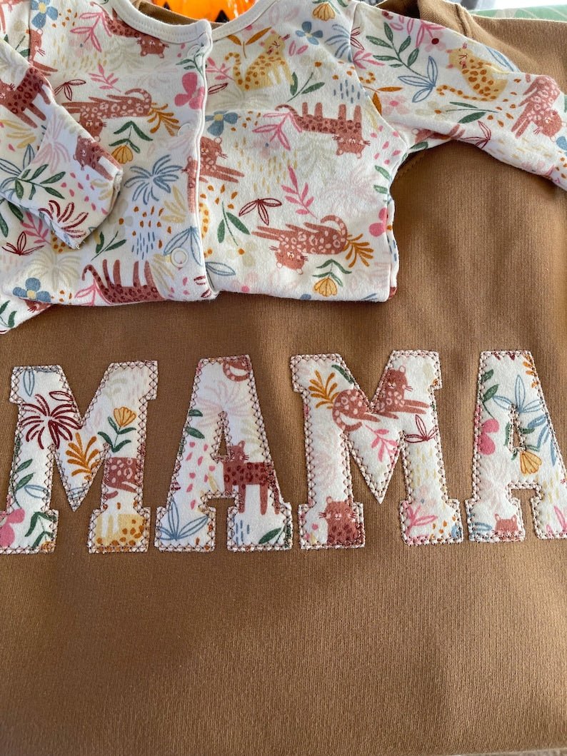 Brown sweatshirt with floral applique “MAMA” design and children's babysuit.