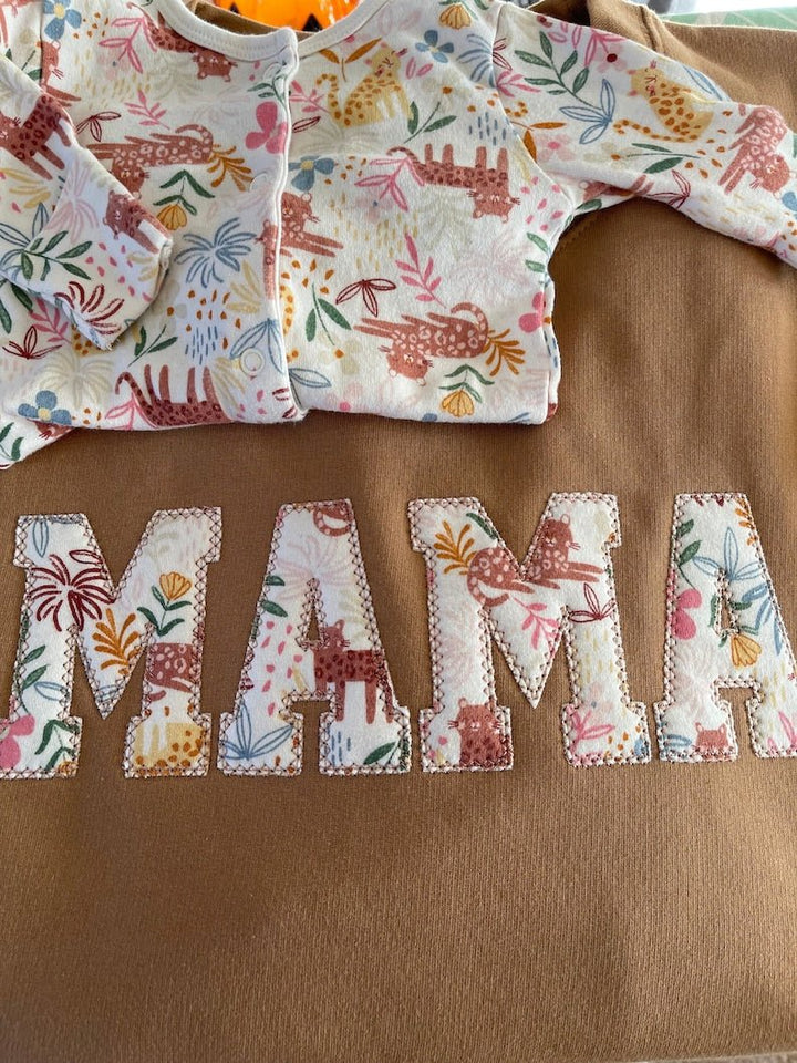 Brown sweatshirt with floral applique “MAMA” design and children's babysuit.
