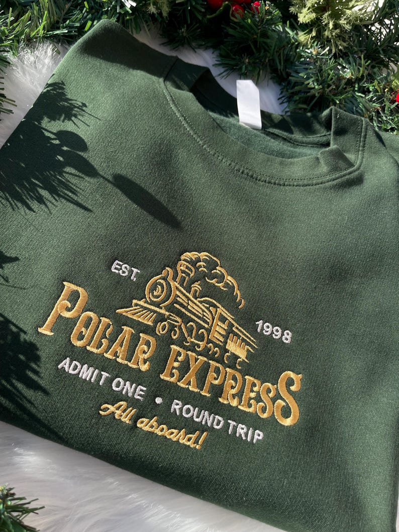 Green sweatshirt with embroidered Polar Express train and ticket design, styled with Christmas garland