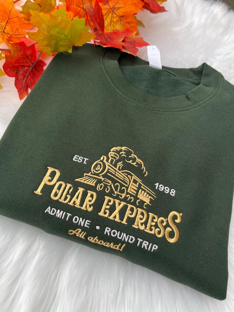 Polar Express embroidered sweatshirt on green fabric, styled with autumn leaves