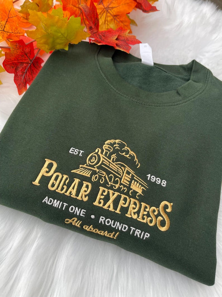 Polar Express embroidered sweatshirt on green fabric, styled with autumn leaves