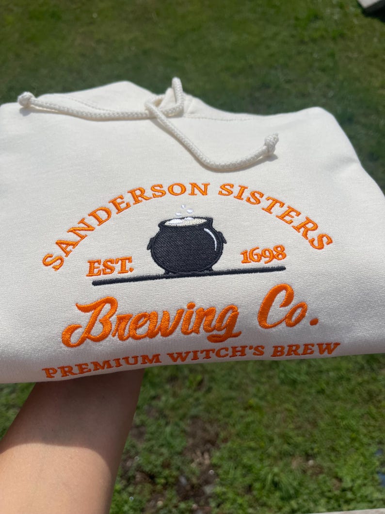 White Sanderson Sisters Brewing Co embroidered hoodie held outdoors