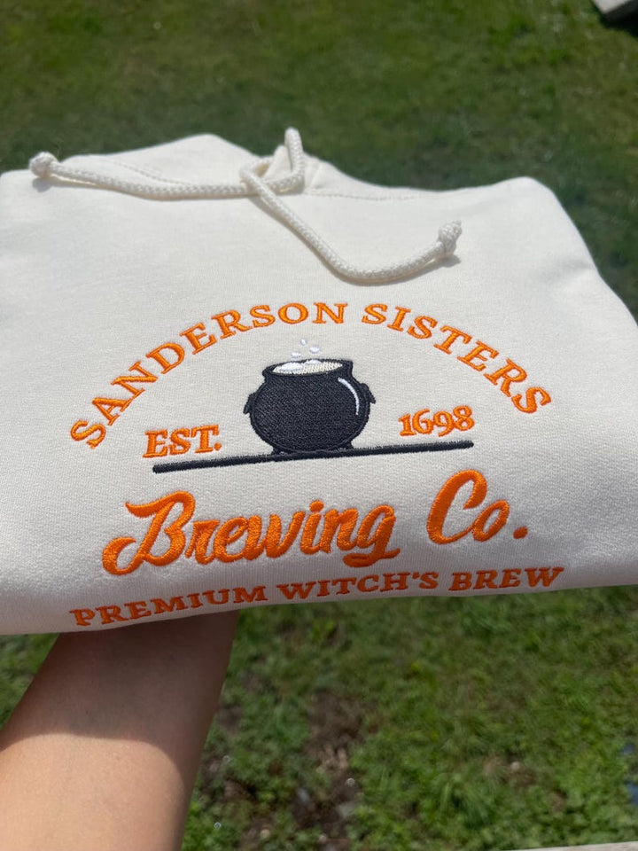 White Sanderson Sisters Brewing Co embroidered hoodie held outdoors
